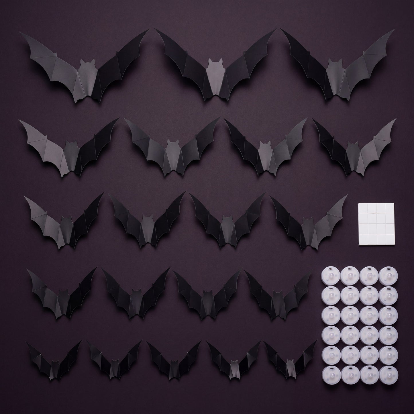 GALLERY. Flat lay of the GlowBats pack contents, matte black bats in five sizes with round LED pucks and adhesive pads