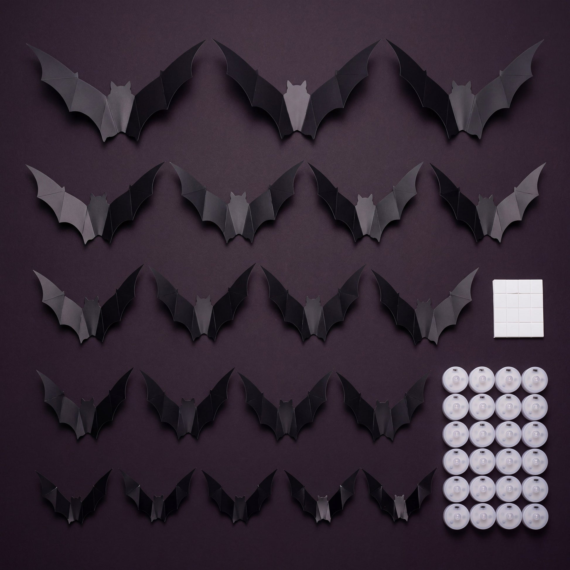 GALLERY. Flat lay of the GlowBats pack contents, matte black bats in five sizes with round LED pucks and adhesive pads