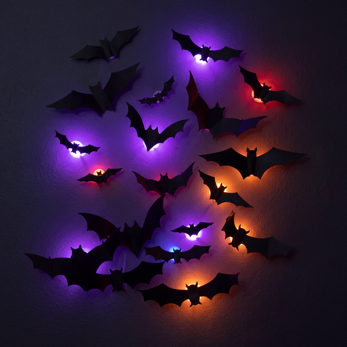 Tight cluster of nine GlowBats on a dark wall at night with overlapping violet, ember orange and deep red halos